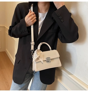 Détail d'un sac beige à rabat avec texture tissée, fermoir métal et anse foulard