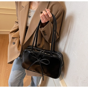 Detail of black bow on shiny leather tote bag shown on a model in a warm setting