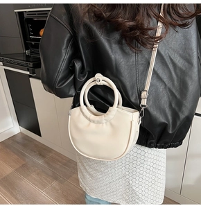 Side view of a beige crescent handbag with a round handle shown in a daily life setting