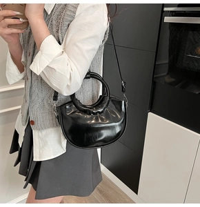Detail view of the black glossy leather crescent bag worn as a stylish crossbody bag