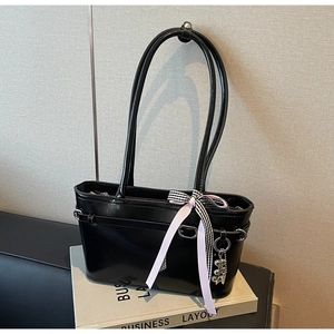 Détail d'un sac cabas en cuir verni noir avec nœud à carreaux et breloque ours argenté