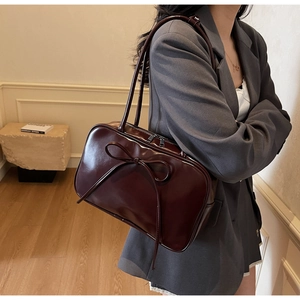 Detail of burgundy patent leather shoulder bag featuring a large bow and glossy finish