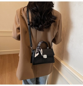 Détail du sac bandoulière noir tissé avec foulard en soie porté par un modèle