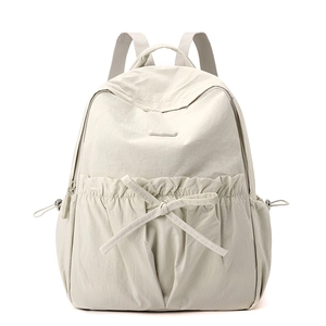 Close-up of cream nylon backpack featuring bow detail and drawstring side pockets
