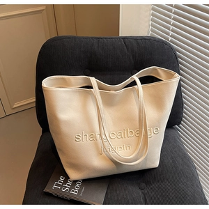 Detailed close-up of a cream canvas tote bag with embossed text on a corduroy sofa