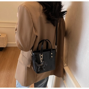 Detail der schwarzen Leder-Eimertasche mit Prägung und Hundeanhänger am Model