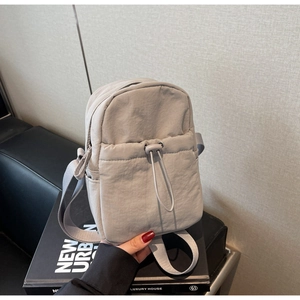 Close-up of light gray nylon crossbody bag with drawstring pocket and adjustable strap