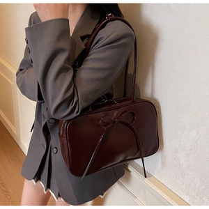 Detail view of burgundy bow shoulder bag worn over a gray blazer for a stylish look