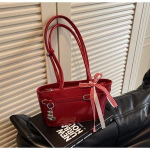 Détail du sac rouge en cuir verni avec pendentif cœur et ruban sur canapé noir