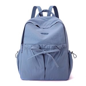 Close-up of blue nylon backpack featuring a decorative bow pocket and drawstring side pouches