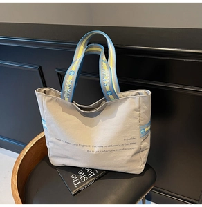 Détail du cabas en toile grise avec bretelles bleu et jaune sur un fauteuil en cuir noir