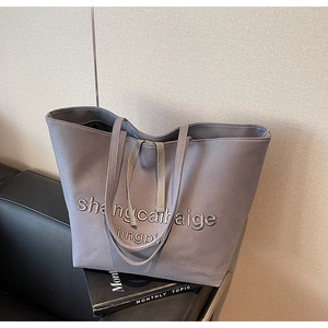 Macro detail of large canvas tote bag with 3D embossed lettering and long shoulder straps