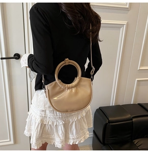 Model view of beige patent leather crescent bag with round handle and slim shoulder strap