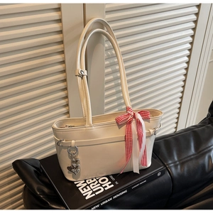 Détail d'un sac cabas blanc crème brillant avec un nœud à carreaux rouges et pendentif cœur