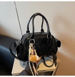 Close-up of black glossy pillow bag featuring embossed letters and a baseball charm