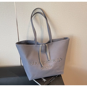 Detail of grey canvas tote bag featuring 3D embroidered text and drawstring closure