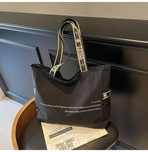 Détail d'un grand sac fourre-tout noir avec lettrage blanc et bandoulière jacquard