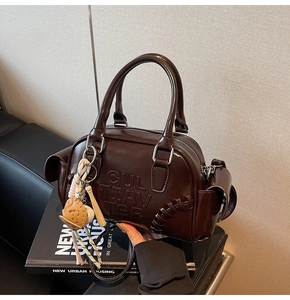 Detail of dark brown Boston bag with embossed logo and baseball charm on books