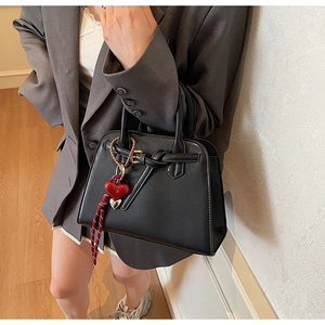 Dettaglio borsa a mano nera con pendente a cuore rosso abbinata a un blazer grigio
