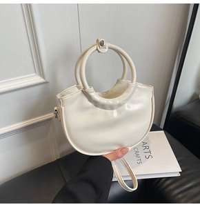Detail of cream crescent handbag with glossy leather finish and metal ring handle