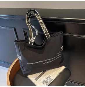 Détail d'un grand sac cabas noir en toile avec imprimé typographique blanc sur une chaise