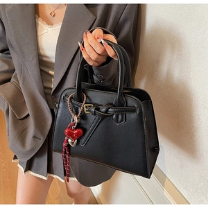Dettaglio di una borsa nera strutturata con fibbia in pelle e ciondolo a cuore rosso