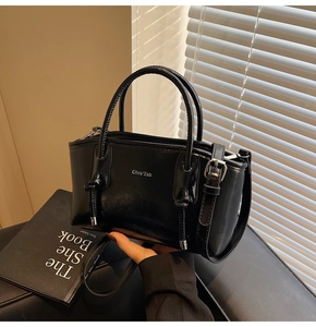 Dettaglio della borsa tote in pelle nera lucida con fibbie in metallo e logo stampato