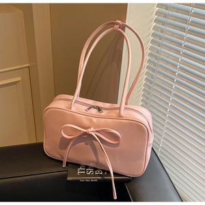 Close-up of a light pink bow shoulder bag on a black leather sofa with natural lighting
