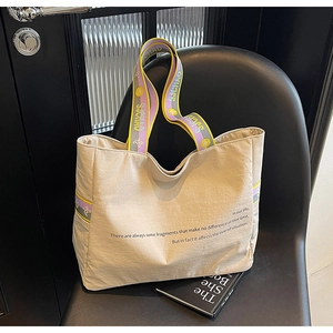Détail du sac cabas en toile beige avec texte graphique et bandoulière tissée colorée