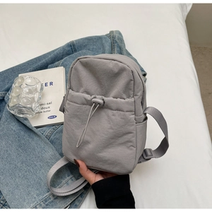 Close-up of light grey nylon crossbody bag with drawstring pocket and adjustable strap