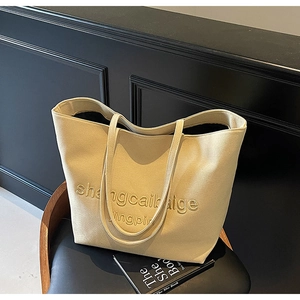Detailed view of a beige canvas tote bag with embroidered text on a black chair