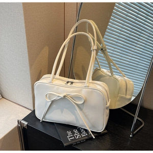 Close-up of cream bow shoulder bag with glossy synthetic leather and dual metal zippers