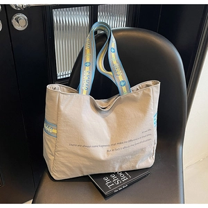 Détail du sac cabas kaki avec des sangles tissées bleu et jaune et une typographie