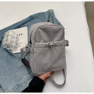 Close-up of light grey quilted nylon crossbody bag with drawstring detail in home setting