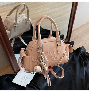 Detail of pink faux leather crossbody bag with embossed letters and baseball charm accessory
