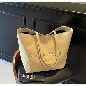 Detail of beige canvas tote bag with embossed lettering placed on a black leather chair