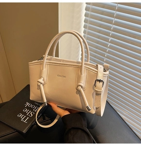 Dettaglio borsa tote in pelle PU crema con manici a nodo e logo del marchio inciso