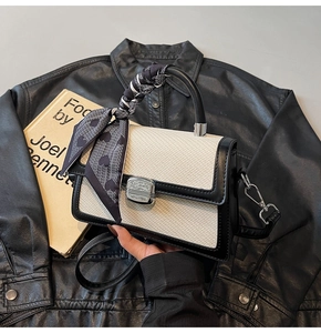 Détail du sac bandoulière contrasté avec texture tressée et poignée ornée d'un foulard