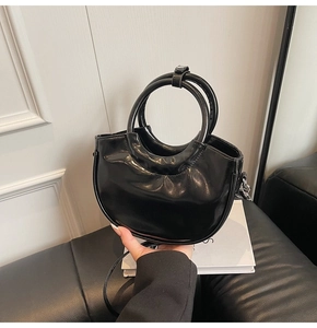 Glossy black patent leather crescent handbag with dual ring handles and shoulder strap