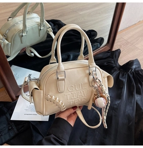 Detail of cream Boston bag with embossed logo and baseball glove charm on silk background