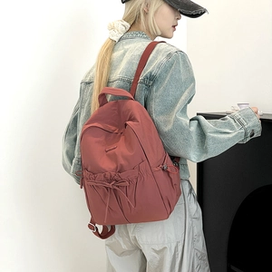 Detail view of brick red nylon backpack featuring drawstring pockets and adjustable straps