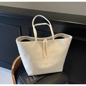 Detail of cream canvas tote bag featuring embossed lettering and decorative strap accents