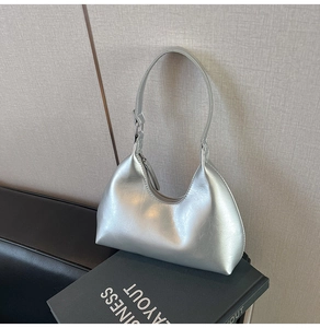 Detail of silver metallic crescent bag with smooth texture placed on a black book