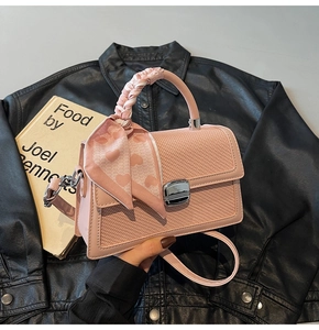 Détail du sac en cuir tressé rose avec foulard à motifs cœur et fermoir rotatif argenté