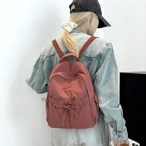Coral nylon backpack featuring drawstring closure and decorative bow on the back of model