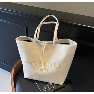 Detail of a beige leather tote bag with embroidered letters on a minimalist chair