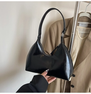 Close-up of black glossy crescent shoulder bag with smooth texture and sleek metal zipper