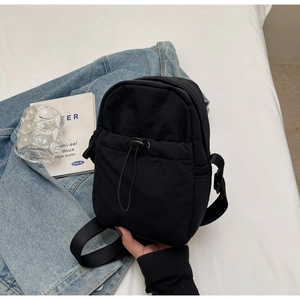 Close-up of black nylon crossbody bag with drawstring on white bedding background
