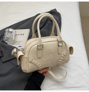 Detail of cream leather shoulder bag featuring baseball stitch accents and embossed text