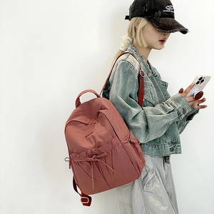 Detail of brick red nylon backpack with drawstring bow and adjustable straps on model